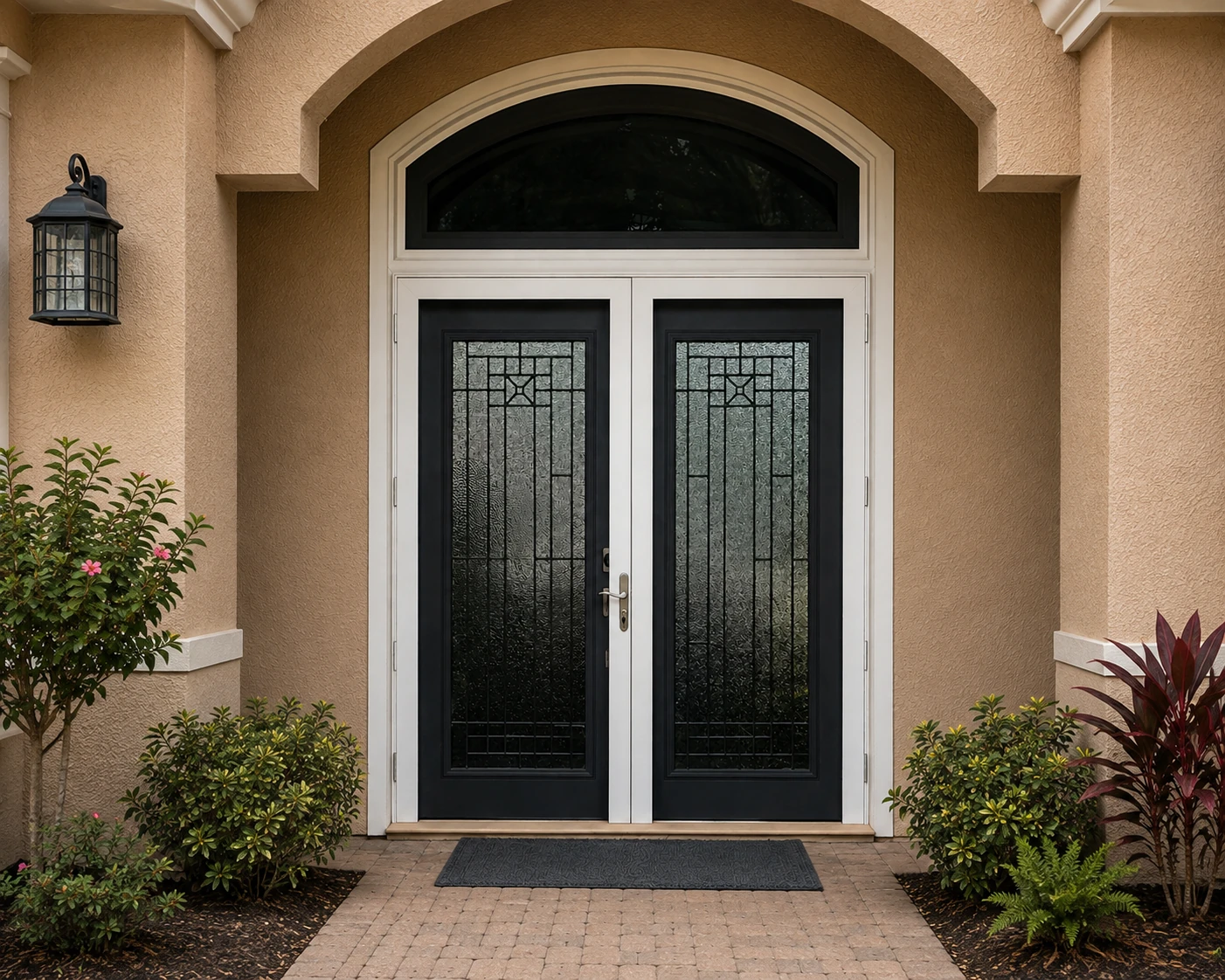 Black double entry doors with decorative glass and an arched transom on a tan stucco Florida home