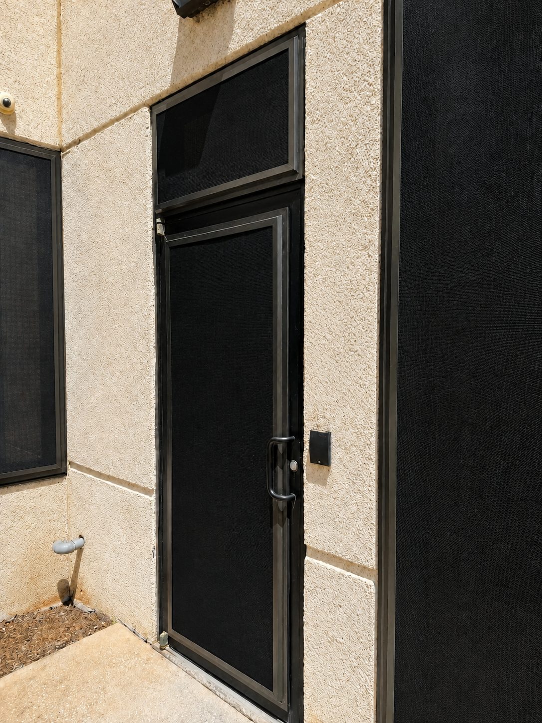 Close view of a commercial entrance protected by a dark Fortress screen door and adjacent screen panels
