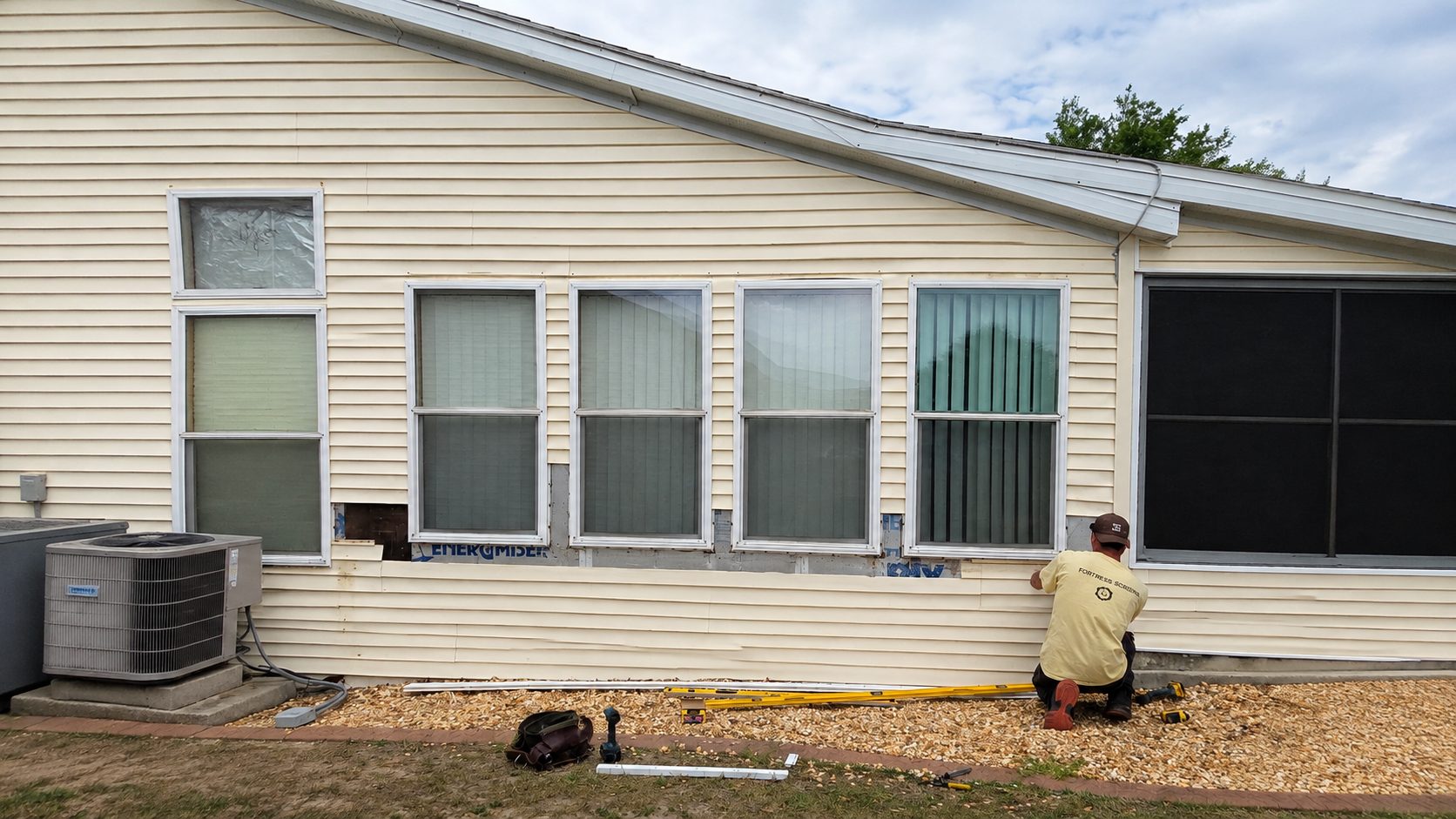 Fortress installer working beside a row of residential windows during a screen installation