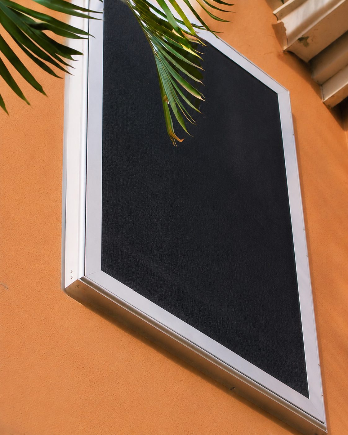 Dark Fortress screen in a silver frame mounted on an orange stucco wall beneath palm fronds